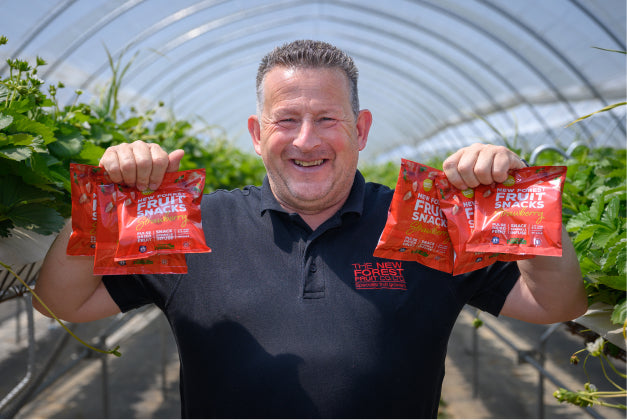 A photo of Sandy from New Forest Fruit Snacks, holding six bags of their dried strawberry snack.